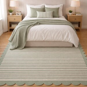 May include: A bedroom scene featuring a bed with white linens, sage green pillows, and a matching throw. Two wooden nightstands flank the bed, each with a lamp and decor. A striped rug with a scalloped edge in sage green and white covers the floor.