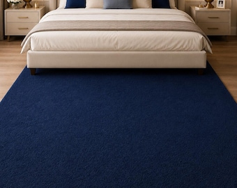 May include: A navy blue area rug in a bedroom setting. The rug is placed in front of a bed with a beige headboard and matching bedding. Two nightstands with lamps flank the bed. A painting hangs above the bed.