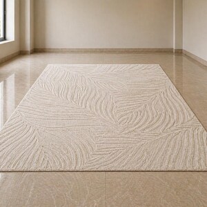 May include: A rectangular beige rug with a textured, leaf-like pattern. The rug is centered on a polished, light-colored floor in a room with neutral walls and a window.