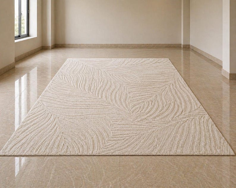 May include: A rectangular beige rug with a textured, leaf-like pattern. The rug is centered on a polished, light-colored floor in a room with neutral walls and a window.