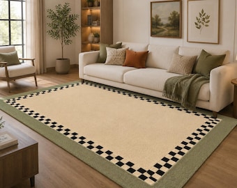 May include: A rectangular area rug featuring a large beige center panel surrounded by a black and white checkered border and an outer sage green frame. The rug has a flat-woven appearance and is positioned on a wooden floor in a living room setting.