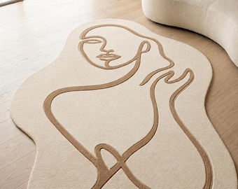 May include: Beige area rug with a brown line drawing of a face and body. The rug has an irregular, organic shape. The design is minimalist and modern, suitable for a living room or bedroom.