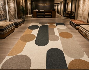May include: A large rectangular area rug featuring a geometric pattern of overlapping circles and rounded oblong shapes in shades of charcoal gray, tan, beige, and cream. The design is printed on a flat surface with a clean, uniform texture.