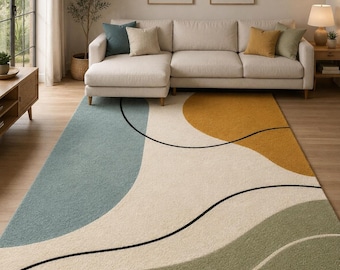 May include: A rectangular area rug featuring an abstract design with large, flowing organic shapes in muted teal, mustard yellow, and sage green against a cream background, accented by thin, sweeping black lines that traverse the surface.