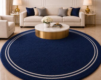 May include: A large, round, navy blue rug with two concentric white stripes near the edge. The rug is the focal point of a living room, with a sofa, coffee table, and side tables with lamps in the background.
