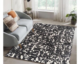 May include: A rectangular area rug with a black and white abstract pattern. The rug is placed on a light-colored wooden floor. The rug's design features a mix of black and white shapes, creating a modern look. The rug is in a living room setting.