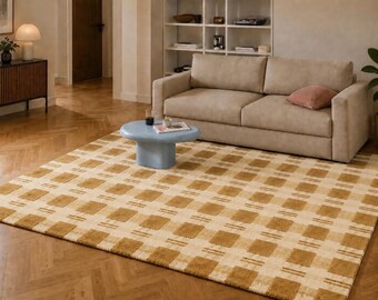 May include: A large, rectangular area rug with a repeating pattern of squares and stripes in shades of beige and brown. The rug is placed on a hardwood floor in a living room setting, with a beige sofa and a blue coffee table.