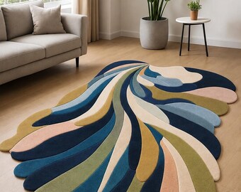 May include: An area rug with an irregular, organic shape featuring a layered, fan-like pattern of curved segments in shades of navy blue, teal, olive green, cream, and soft peach, creating a dynamic, flowing composition across the floor surface.