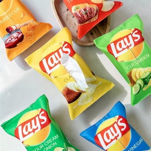 Könnte beinhalten: Eine Sammlung von Serviettenbox-Hüllen, die wie Lay's-Kartoffelchips-Tüten aussehen. Die Hüllen zeigen verschiedene Geschmacksrichtungen, darunter Classic, Barbecue, Gurke, Sauerrahm & Zwiebel und Essig, mit dem Lay's-Logo.