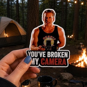 May include: A die-cut vinyl sticker featuring a man in a black tank top with the text PERKIS POWER, holding a camera. Below the figure, the text reads YOU'VE BROKEN MY CAMERA in white and red block letters against a black background with a white border.