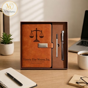 May include: A brown leather journal with a silver clasp, a pen, and a pen refill, presented in a gift box. The journal features a scales of justice graphic and the text "Victoria Elise Monroe, Esq. University School of Law Class of 2026 JD."