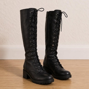 May include: A pair of knee-high black boots featuring a full-length front lace-up closure with dark metal eyelets, a rounded toe, a block heel, and a lugged rubber sole. The boots have a smooth finish and black laces tied at the top.