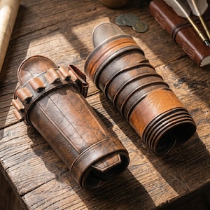 May include: Two brown leather quivers, one with a series of small pockets and the other with a layered design. The quivers are on a wooden surface, with sunlight casting shadows. The leather has a distressed, vintage appearance.