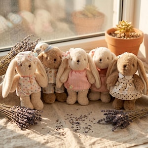 May include: A group of soft toy bunny and teddy bear dolls. The bunnies have long ears and wear dresses or outfits. The teddy bear wears pyjamas. The dolls are in various colours, including pink, white, and brown. The dolls are arranged on a light-coloured surface.