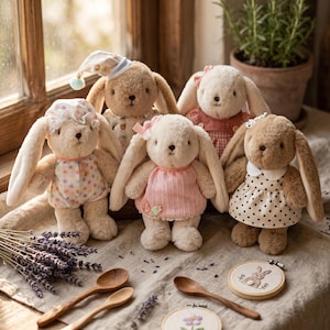 May include: A group of soft toy bunny rabbits, each dressed in different outfits such as dresses and pyjamas. The bunnies are beige and white, with long ears and embroidered faces. Accessories include lavender, wooden spoons, and embroidered hoops.