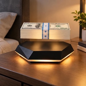 Peut inclure: Une pile de billets de cent dollars en lévitation, maintenue par une bande de papier blanc ornée d'étoiles bleues, flottant au-dessus d'une base hexagonale noire à facettes émettant une lumière chaude par son bord inférieur.