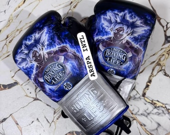 Op de afbeelding: Een paar zwarte bokshandschoenen met een blauwe afbeelding van een anime-personage met stekelig haar. De handschoenen tonen de tekst "NO BOXING NO LIFE" en "HECHO EN MEXICO" met een zilveren polsgedeelte met het opschrift "BOXING LIFE SQUAD".