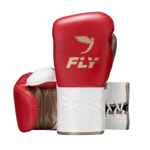 Op de afbeelding: Een paar rood-witte bokshandschoenen met een goudkleurig logo van een gevleugeld figuur boven de tekst FLY. De handschoenen hebben een witte polsmanchet met een vetersluiting aan de achterkant en een binnenvoering in metallic brons.