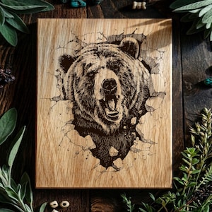 May include: A rectangular wooden plaque featuring a dark, detailed laser-engraved illustration of a grizzly bear head. The bear appears to be breaking through the surface of the wood, with cracked, jagged edges surrounding the animal's face.