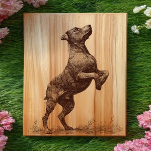 May include: A rectangular wooden plaque featuring a dark brown laser-engraved illustration of a dog standing on its hind legs. The dog is depicted in profile, looking upward with its front paws raised. The wood grain is visible throughout the surface.