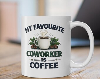 May include: A white ceramic mug featuring a graphic illustration of a steaming cup of coffee surrounded by green leaves and coffee beans. The text printed on the mug reads, "MY FAVOURITE COWORKER IS COFFEE," with decorative stars and horizontal lines.
