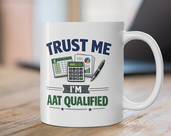 May include: A white ceramic mug featuring the dark blue text TRUST ME and the green text I'M AAT QUALIFIED. Between the text lines is a graphic illustration of a green spreadsheet, a calculator, a colorful pie chart document, and a pen.