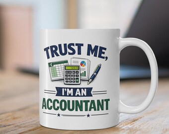 May include: A white ceramic mug featuring the dark blue text "TRUST ME," and the green text "I'M AN ACCOUNTANT." Between the lines of text is a graphic illustration of a calculator, a pen, and financial documents with a colorful pie chart.