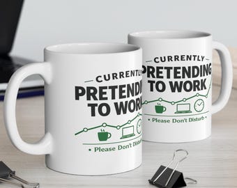 May include: Two white ceramic mugs featuring the black text "CURRENTLY PRETENDING TO WORK" and "Please Don't Disturb" in green. The design includes a green line graph, a coffee mug icon, a laptop icon, and a clock icon printed on the front.