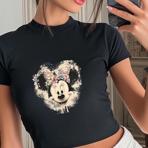 May include: Black crop top featuring a Minnie Mouse graphic. The graphic is a heart-shaped design with Minnie's face and a floral bow. The shirt has short sleeves and a mock neck. The text "COLOR: BLACK GILDAN" is in the upper right corner.