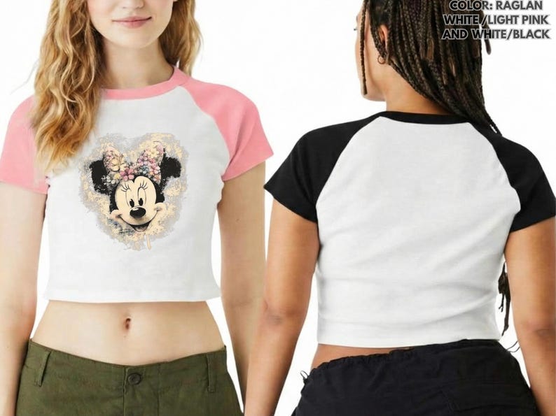 May include: White crop top with pink raglan sleeves featuring a Minnie Mouse graphic. The graphic is a heart-shaped design with Minnie's face and a floral bow. The back of the shirt is white with black raglan sleeves.