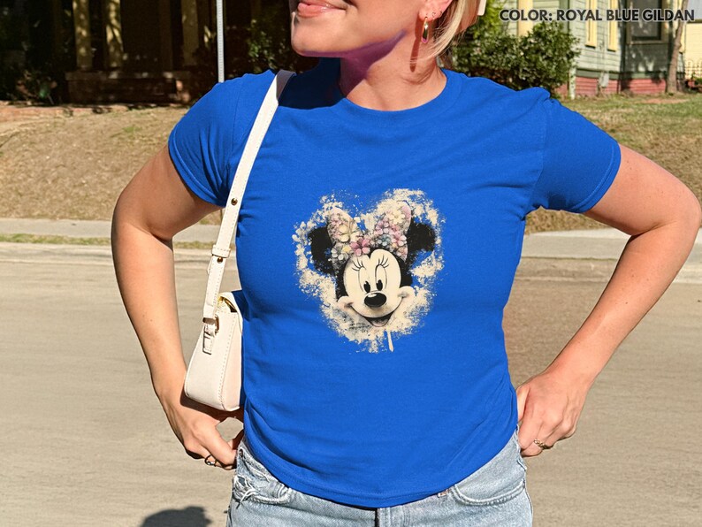 May include: Royal blue t-shirt featuring a Minnie Mouse graphic with a floral design. The graphic is centered on the shirt and includes a white and beige background. The shirt has short sleeves and a crew neck.