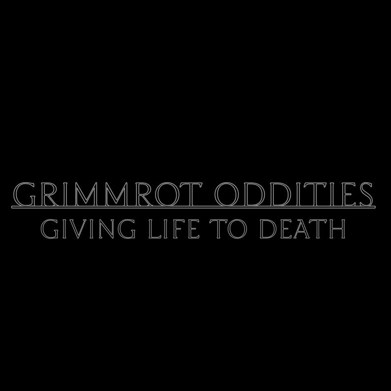 May include: A black graphic design featuring the white outlined text GRIMMROT ODDITIES underlined with a horizontal line, followed by the text GIVING LIFE TO DEATH in a matching white outlined font centred on a solid black background.