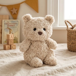 May include: A plush, beige teddy bear with a textured, fluffy appearance. The bear has black eyes and a brown nose. It is sitting on a neutral-colored surface, with a children's book and wooden blocks in the background. A decorative banner hangs above.