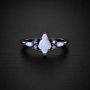 Könnte beinhalten: Ein Ring aus schwarzem Metall mit einem zentralen, drachenförmigen, irisierenden Opal, flankiert von zwei kleineren marquise-geschliffenen Opalen und vier runden violetten Akzentsteinen. Das Band ist dünn und dunkel und bildet einen Kontrast.