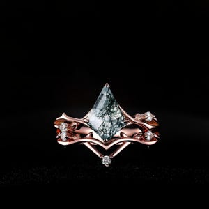 Könnte beinhalten: Ein Ring aus Roségold mit einem drachenförmigen Moosachat-Mittelstein mit dunkelgrünen Einschlüssen. Die Ringschiene hat ein astähnliches Design, das mit kleinen, klaren, rund geschliffenen Steinen besetzt ist, die entlang der Metallkurven liegen.