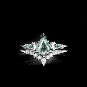Könnte beinhalten: Ein silbernes Ring-Set mit einem großen, smaragdgrünen Edelstein mit einem einzigartigen, geometrischen Schliff. Der Ring ist mit kleineren, klaren Edelsteinen und einem zarten Band akzentuiert, was ein elegantes Design ergibt. Das Set enthält ein passendes Band.