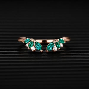 Op de afbeelding: Een open ring van roségoud met twee symmetrische clusters van marquise-geslepen groene stenen en kleine ronde heldere stenen. De ringband is gepolijst en gebogen, met de decoratieve elementen in een waaierpatroon aan beide zijden.