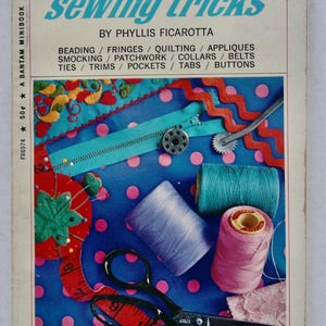 May include: A vintage sewing book titled "sewing tricks" by Phyllis Ficarotta. The cover features sewing notions like thread spools, scissors, a zipper, and a measuring tape. The background is a blue fabric with pink polka dots.