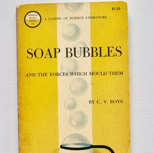 May include: A yellow book cover with the title "SOAP BUBBLES" and the subtitle "AND THE FORCES WHICH MOULD THEM". The book is part of the Science Study Series and is by C. V. Boys. The cover features a drawing of a soap bubble being held by a pair of tongs.