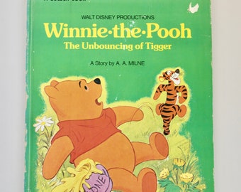 Puede incluir: Una cubierta de libro verde con el título "Winnie de Pooh El rebote de Tigger" y una historia de A.A. Milne. La cubierta presenta una ilustración de Winnie de Pooh sosteniendo una olla de miel y Tigger rebotando en el fondo.