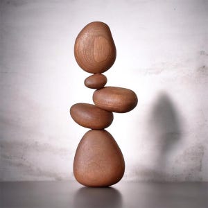 May include: A vertical sculpture composed of five smooth, rounded wooden forms stacked in a balanced arrangement. Each piece features a natural brown wood grain texture, varying in size and shape, creating a singular, cohesive, and upright structure.