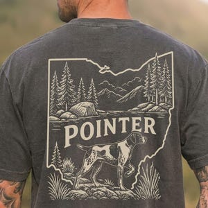 May include: Dark gray t-shirt featuring a graphic of a Pointer dog within an outline of a state, with trees, mountains, and the word "POINTER". The design is in a vintage style, with a faded appearance.