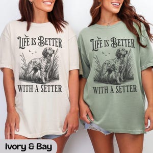 May include: Two t-shirts, one ivory and one bay green, with the text "Life is Better With a Setter." The graphic features a detailed illustration of a setter dog in tall grass. The shirts are a relaxed fit.