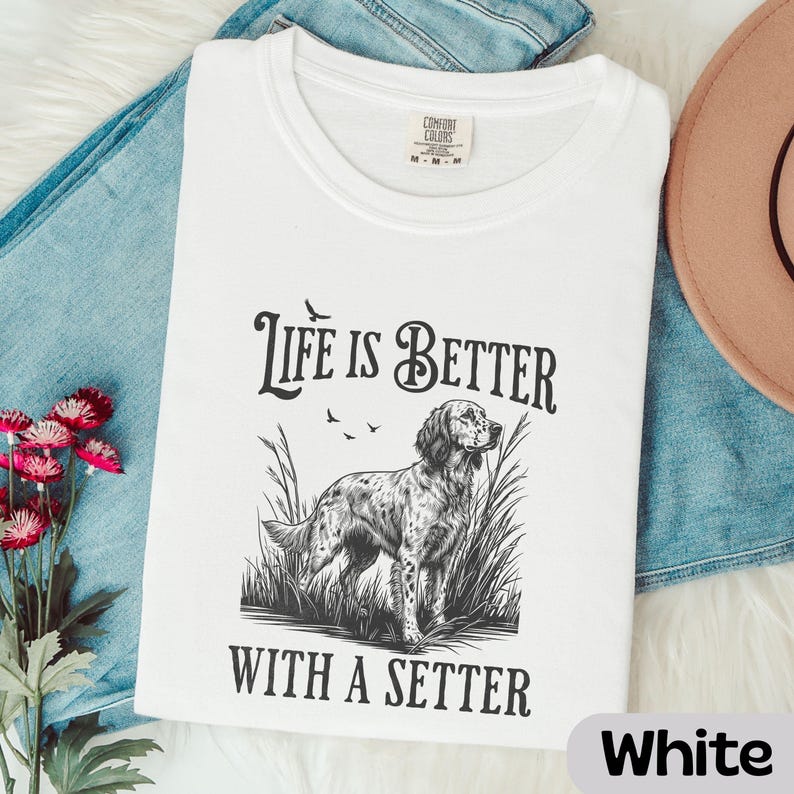 May include: White t-shirt with the text "Life is Better With A Setter" and a graphic of a setter dog in tall grass. The shirt is a Comfort Colors brand and is folded on top of blue jeans.