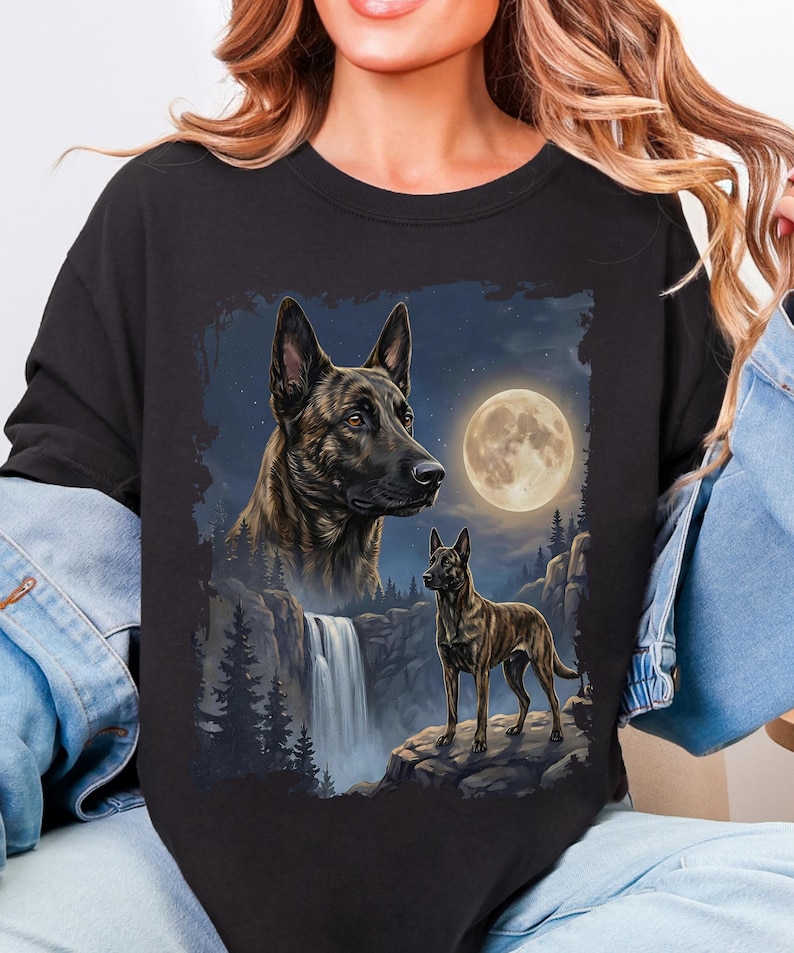 May include: Black sweatshirt featuring a detailed illustration of a dog with a waterfall, full moon, and forest scene. The dog is brown and black with a focused expression. The background includes a night sky with stars.