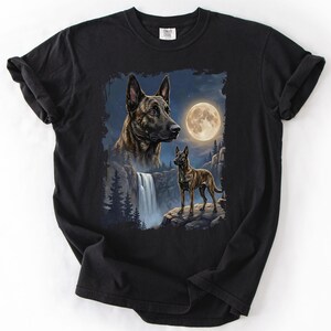 May include: Black t-shirt featuring a detailed illustration of two dogs, one a close-up of the head and the other standing on a rock. The background includes a waterfall, trees, and a full moon.