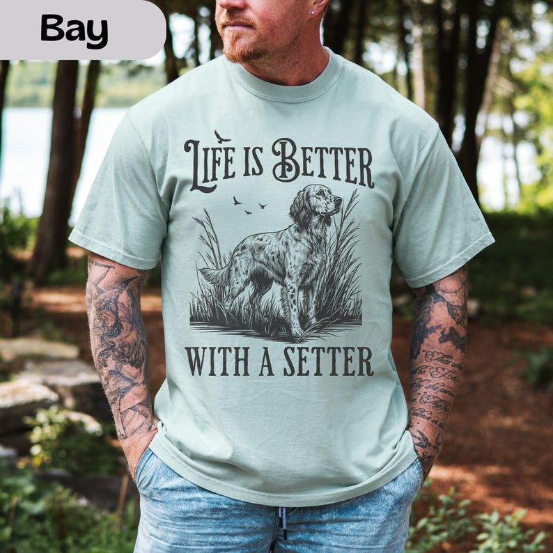 May include: A light green t-shirt with the text "LIFE IS BETTER WITH A SETTER" in black. The graphic features a setter dog standing in tall grass. The shirt is short-sleeved and made of a soft material.