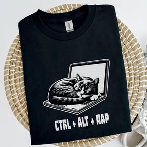May include: Black t-shirt with a white graphic of a cat sleeping on a laptop. The text "CTRL + ALT + NAP" is printed below the cat.