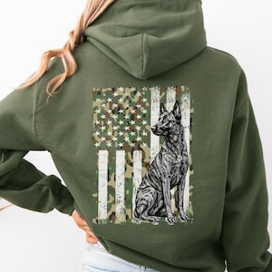 May include: Olive green hoodie featuring a distressed American flag design with a camouflage pattern and a seated dog illustration. The dog is black and white. The hoodie has a hood and long sleeves.