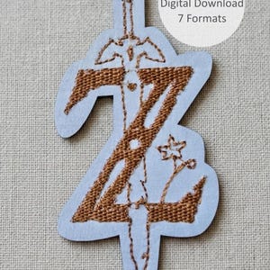 Pode incluir: Um design de bordado com uma letra Z grande castanha com uma espada integrada no traço vertical e um pequeno motivo floral à direita. O design está sobre um fundo azul claro com o texto 3 sizes Digital Download 7 Formats.